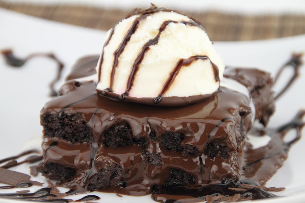 A slice of chocolate cake topped with a scoop of vanilla ice cream drizzled with chocolate cake. 