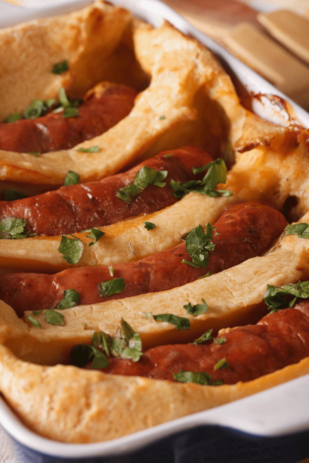 Sausages covered with baked pudding batter and garnished with chopped parsley serve on a casserole