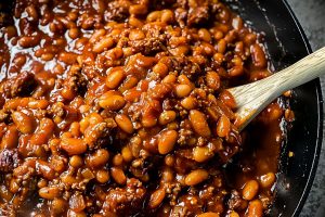 BBQ Baked Beans in a Cast Iron Skillet with a Wooden Spoon
