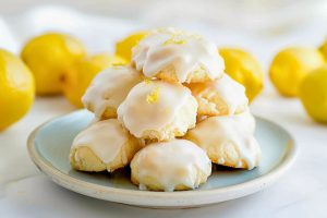 Pile of Lemon Drop Cookies with Lemon Icing on a Plate with Fresh Lemons in the Background
