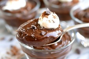 Close Up of Spoonful of Chocolate Cornstarch Pudding with a Dollop of Whipped Cream and More Glass Ramekins of Pudding in the Background