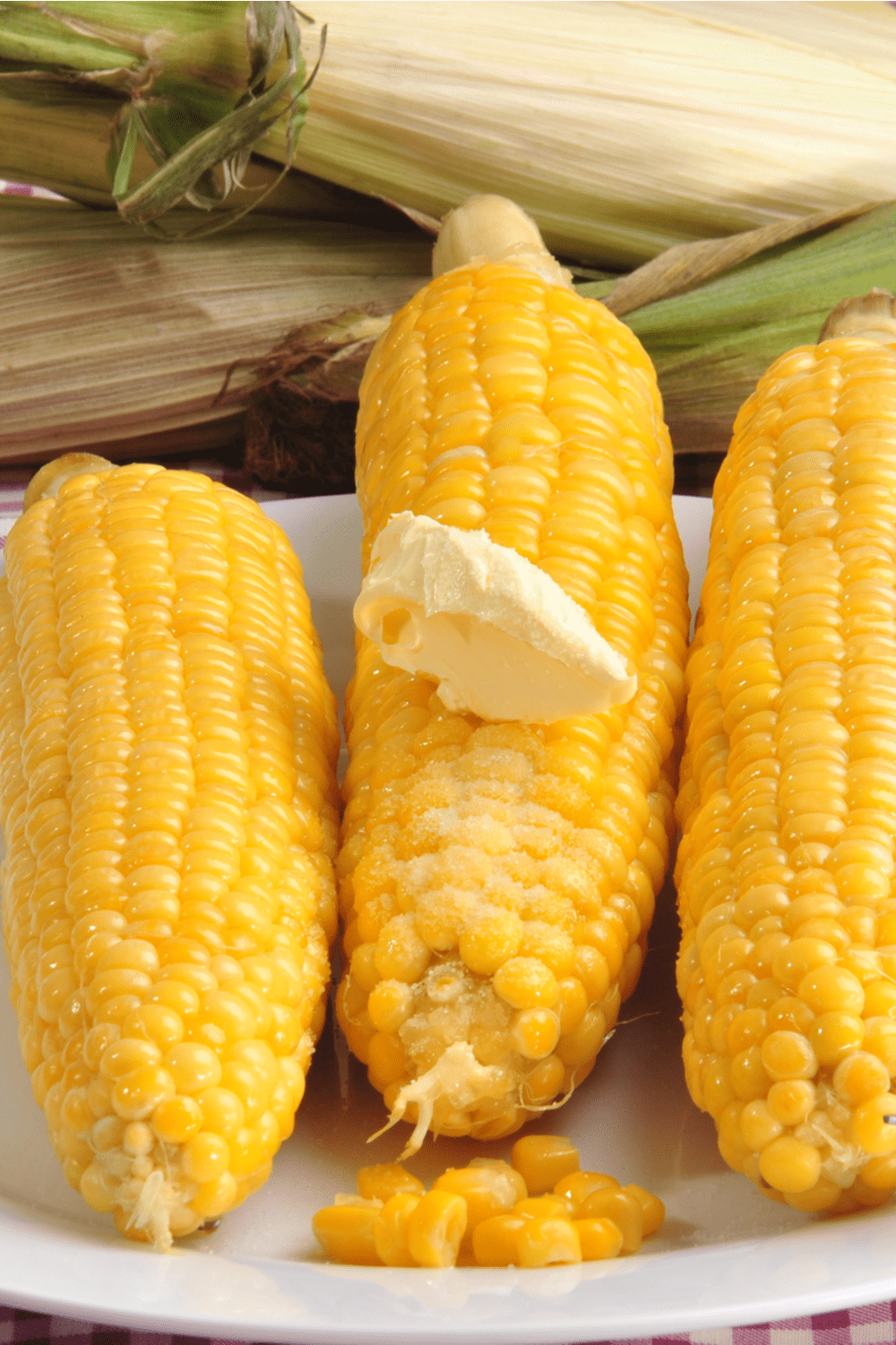 Three cooked yellow corn with a piece of butter served on white plate.