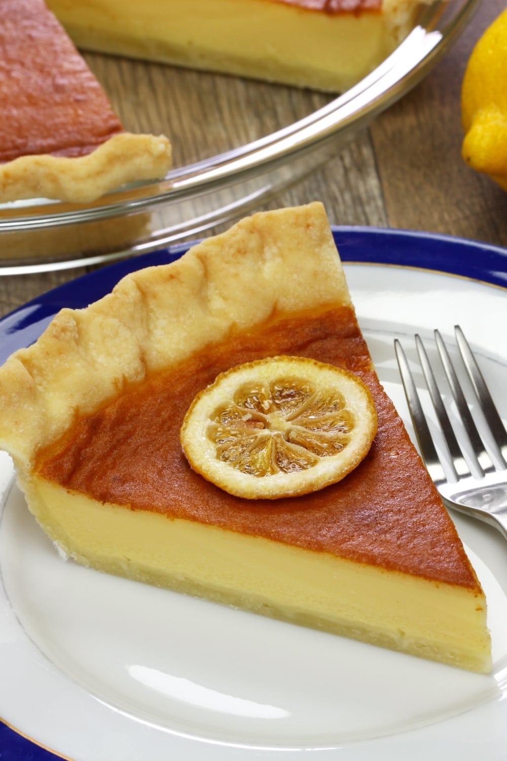 Slice of Buttermilk Pie with Lemon Slice on top served on a plate with fork, 