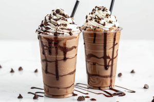 Two Plastic Cups of Starbucks Double Chocolate Chip Frappuccinos with Whipped Cream, Chocolate Drizzle, and Chocolate Chips