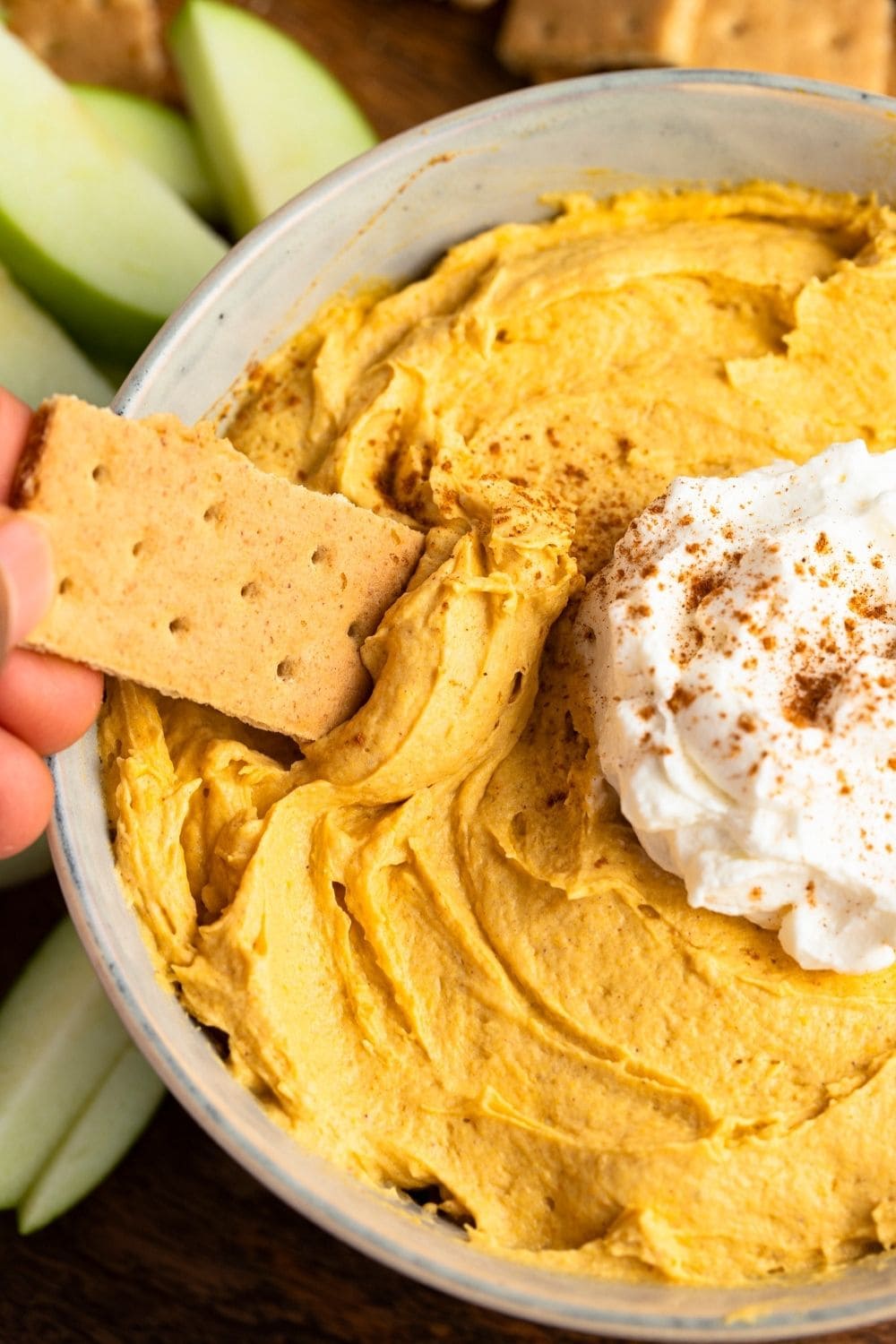 Cracker dipped in creamy pumpkin dip on a bowl with whipped cream on top. 