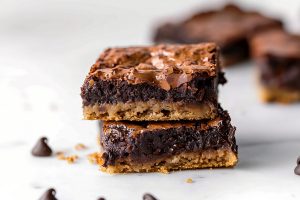 Two Stacked Gooey, Fudgy Brookies with Brownie Top Layer and Chocolate Chip Cookie Bottom Layer on a White Marble Table with Chocolate Chips Around the Brownies