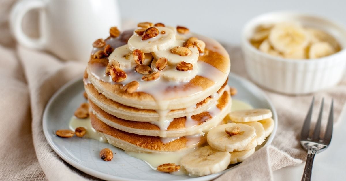 A Stack of Pancakes with Condensed Milk, Banana Slices and Pecan Nuts