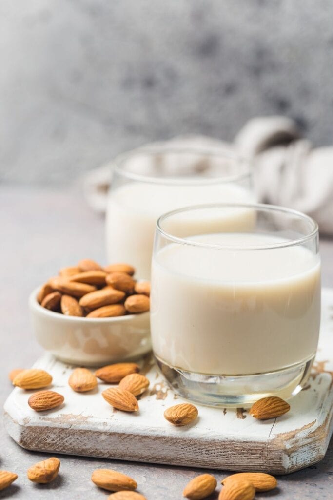 Almond Milk in a glass next to Almond in a small bowl