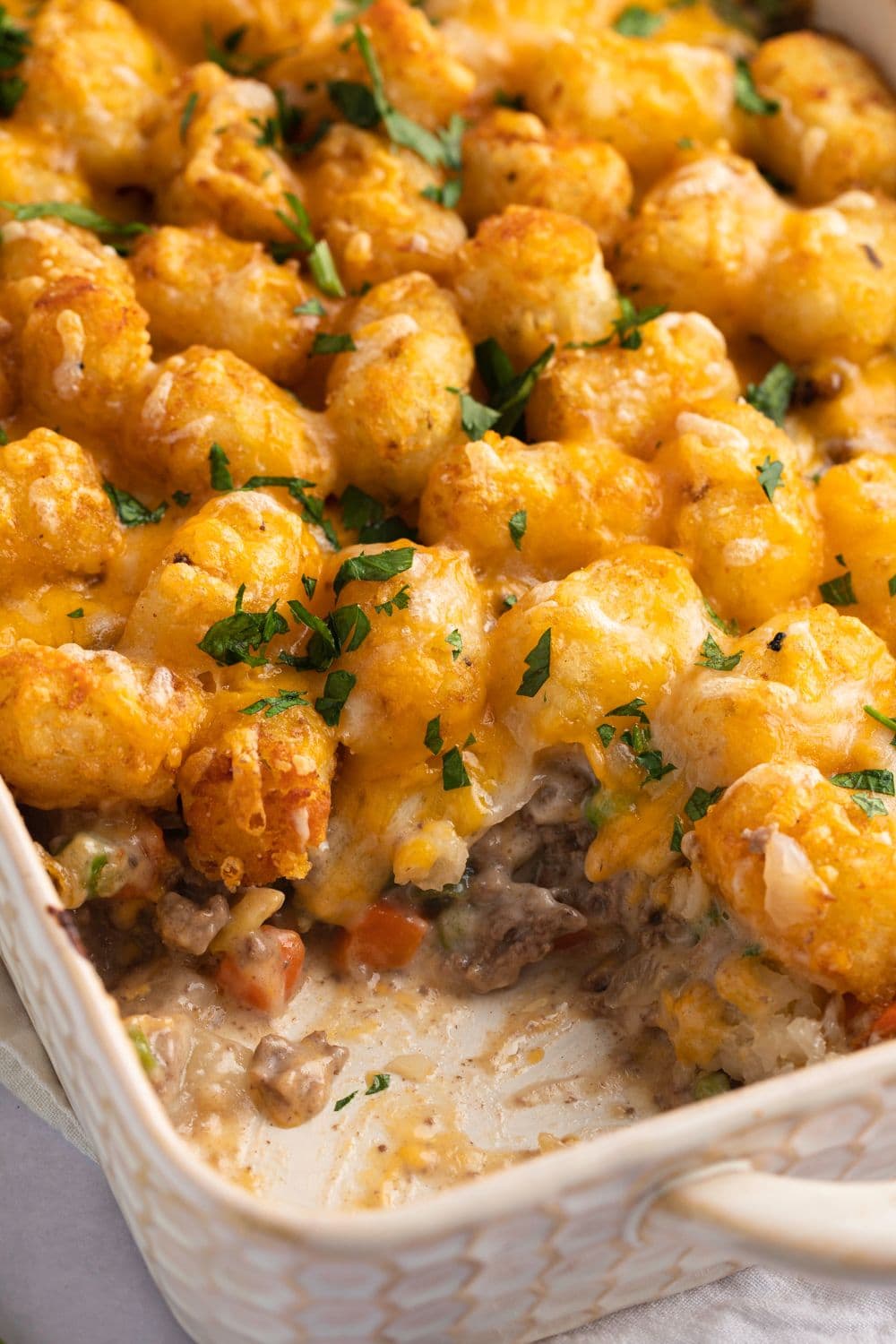 Tater Tot Casserole with Ground Beef and topped with lots of cheddar cheese, garnished with chopped parsley served on a casserole