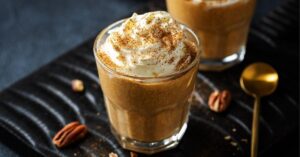 A Glass of Pumpkin Spice Latte with Whipped Cream, Cinnamon and Pecan Nuts