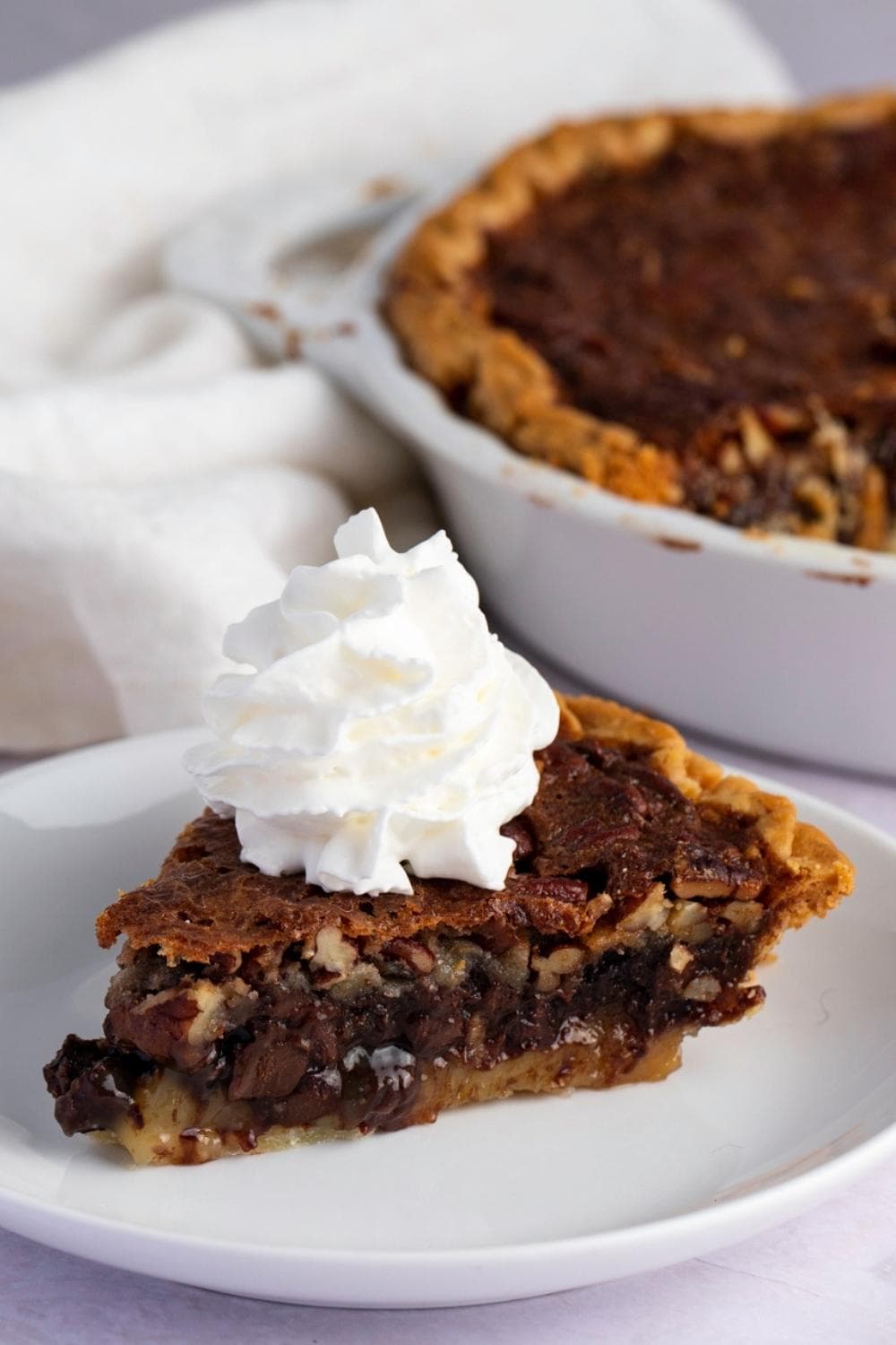 A slice of pie with chocolatey pecan filling and pump of whipped cream on top.