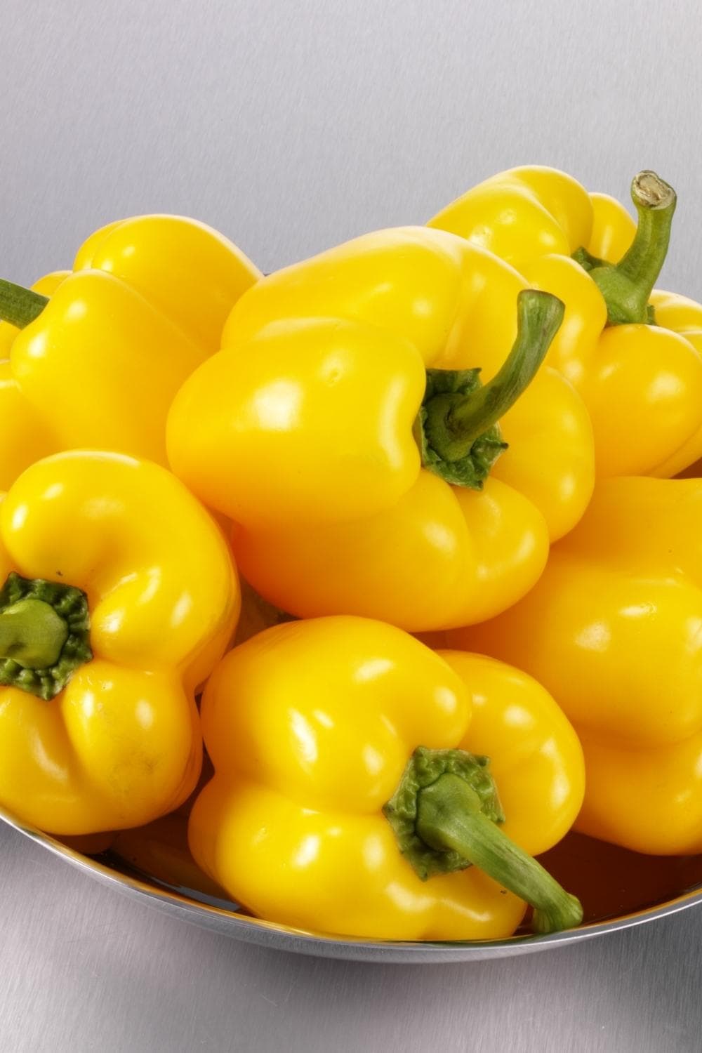 Stainless bowl filled with ripe yellow, shiny skinned bell peppers. 