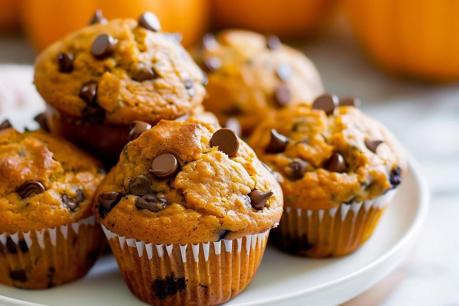 Close Up of Pumpkin Chocolate Chip Muffins, Stacked on a Plate with Pumpkins in the Background