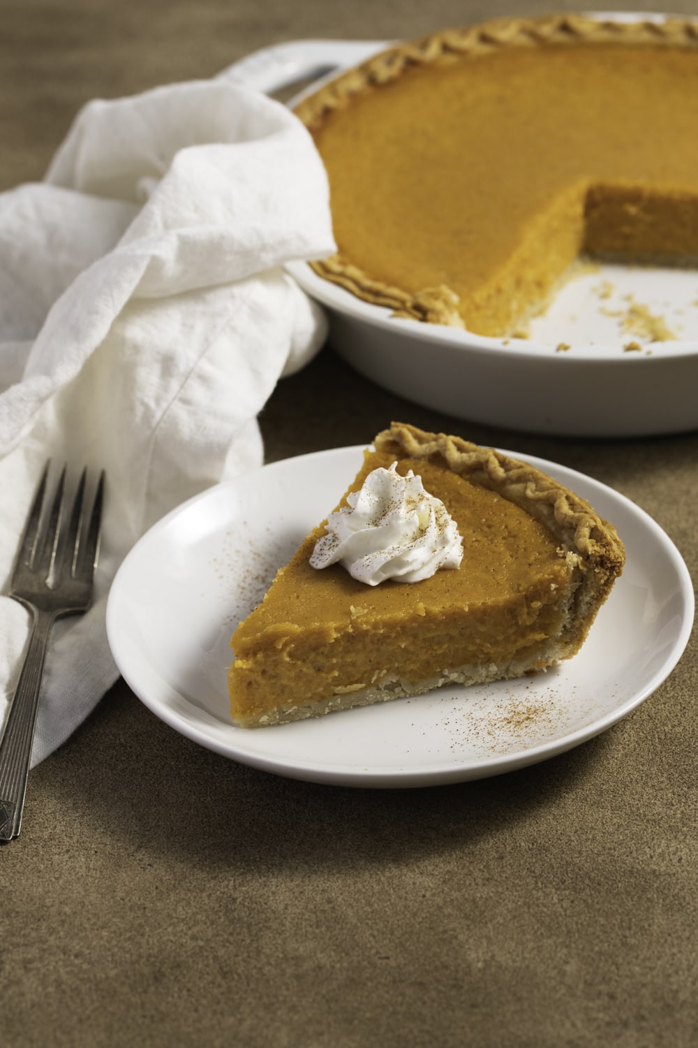 A serving of sweet potato pie slice with pump of whipped cream on top. 