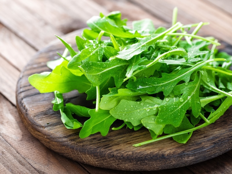 Arugula leaves on a wooden chopping board.