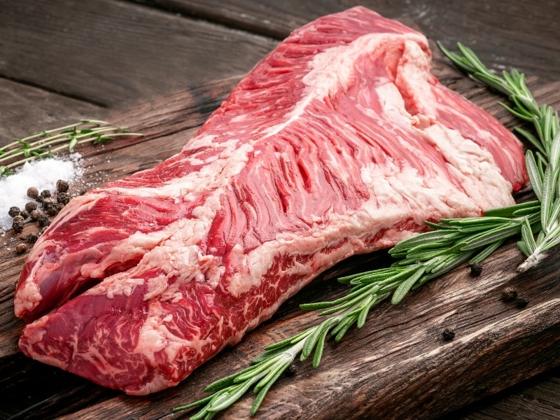 Raw Hanger Steak on a Wooden Cutting Board with Thyme and Rosemary