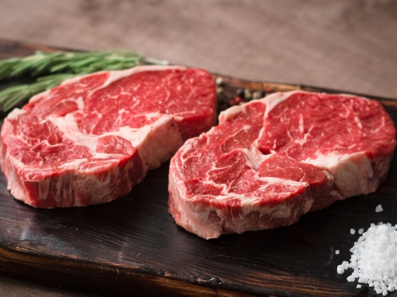 Two Fresh Raw Ribeye on a Wooden Cutting Board with Salt and Pepper