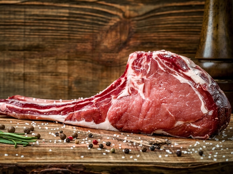 Raw Tomahawk on a Wooden Board with Salt and Pepper