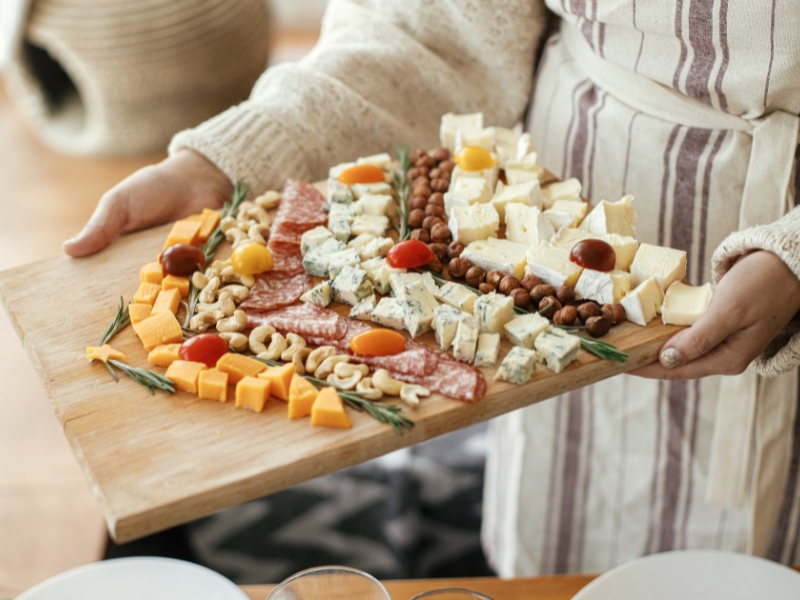 A Person Holding a Charcuterie Board With Variety of Cheese and Salami Appetizers 