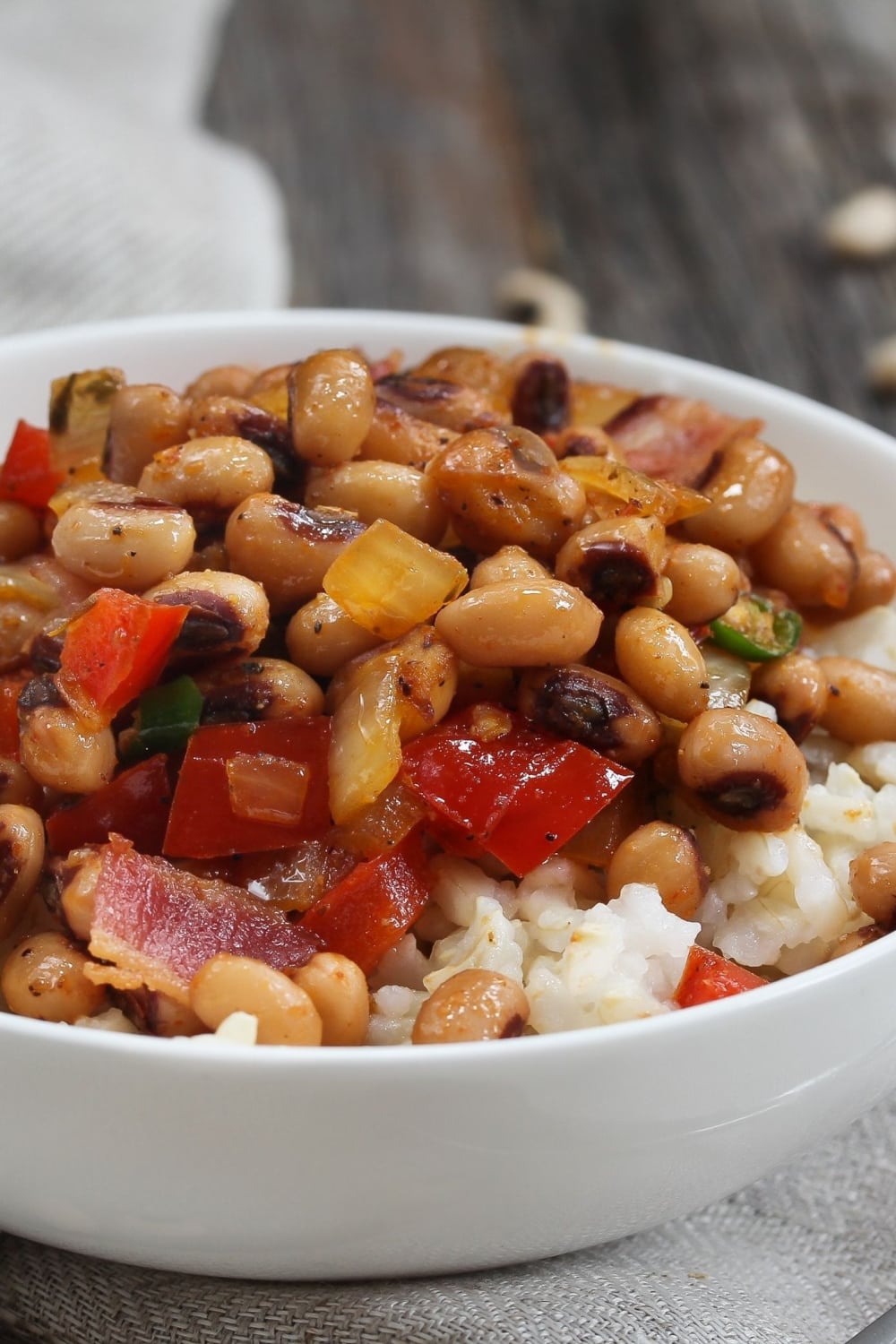 Hoppin’ John with bacon, Andouille sausage, peppers, chilis, and Cajun seasoning topped on white rice in a bowl. 