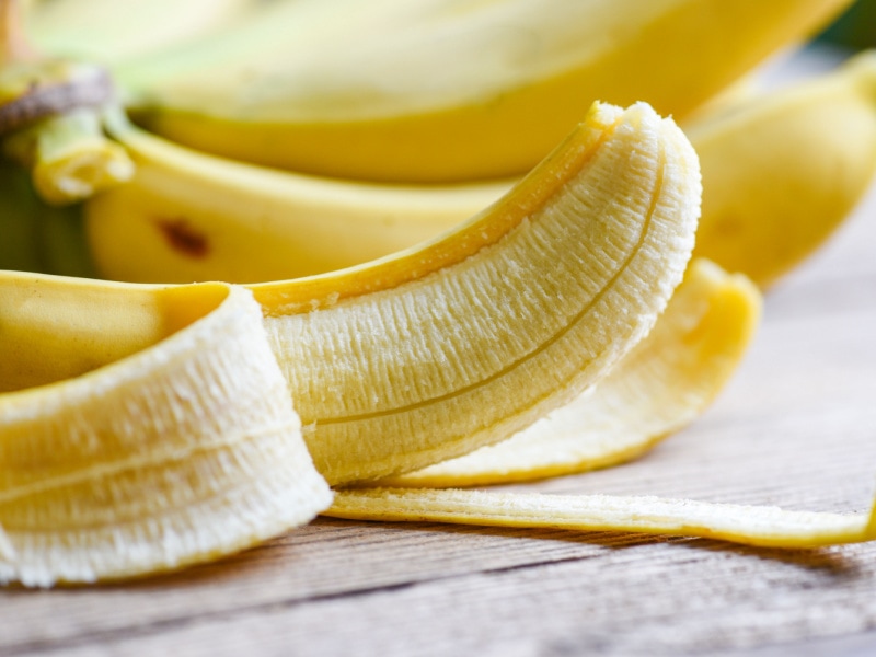 Half peeled ripe yellow banana lying on a wooden table