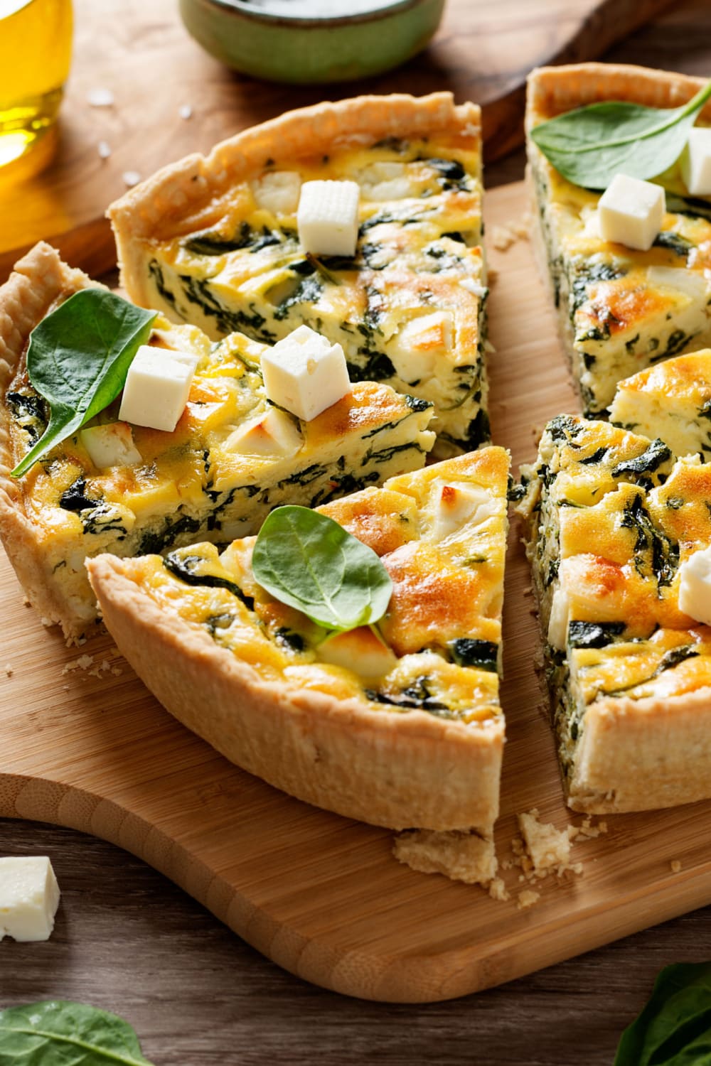 Sliced whole spinach quiche on top of wooden board topped with
