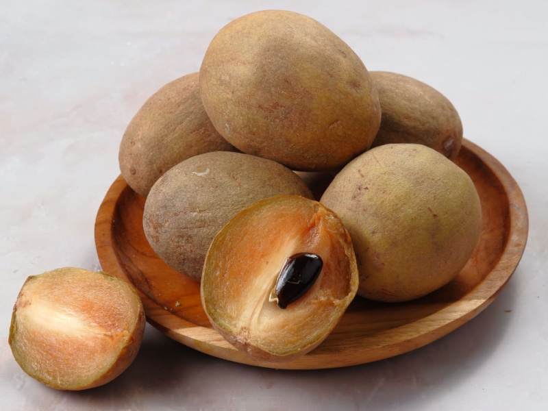 Sapodilla Whole and Slice on a Wooden Plate
