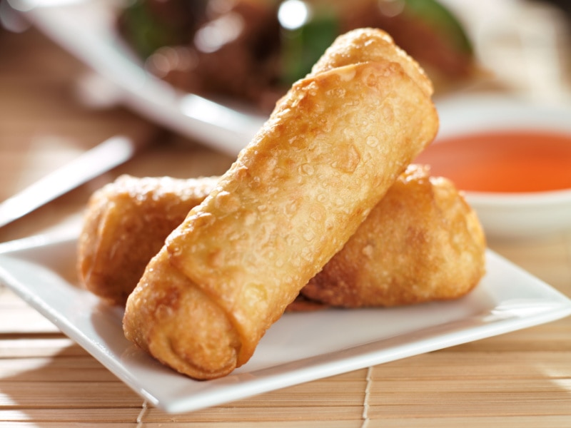 Two pieces of fried spring rolls served on a square saucer. 