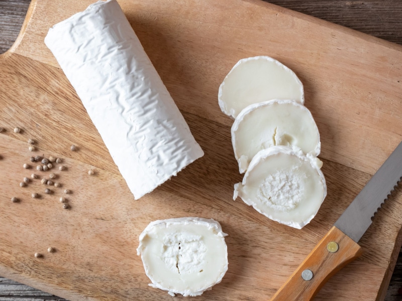 Whole and Sliced Goat Cheese on a Wooden Cutting Board