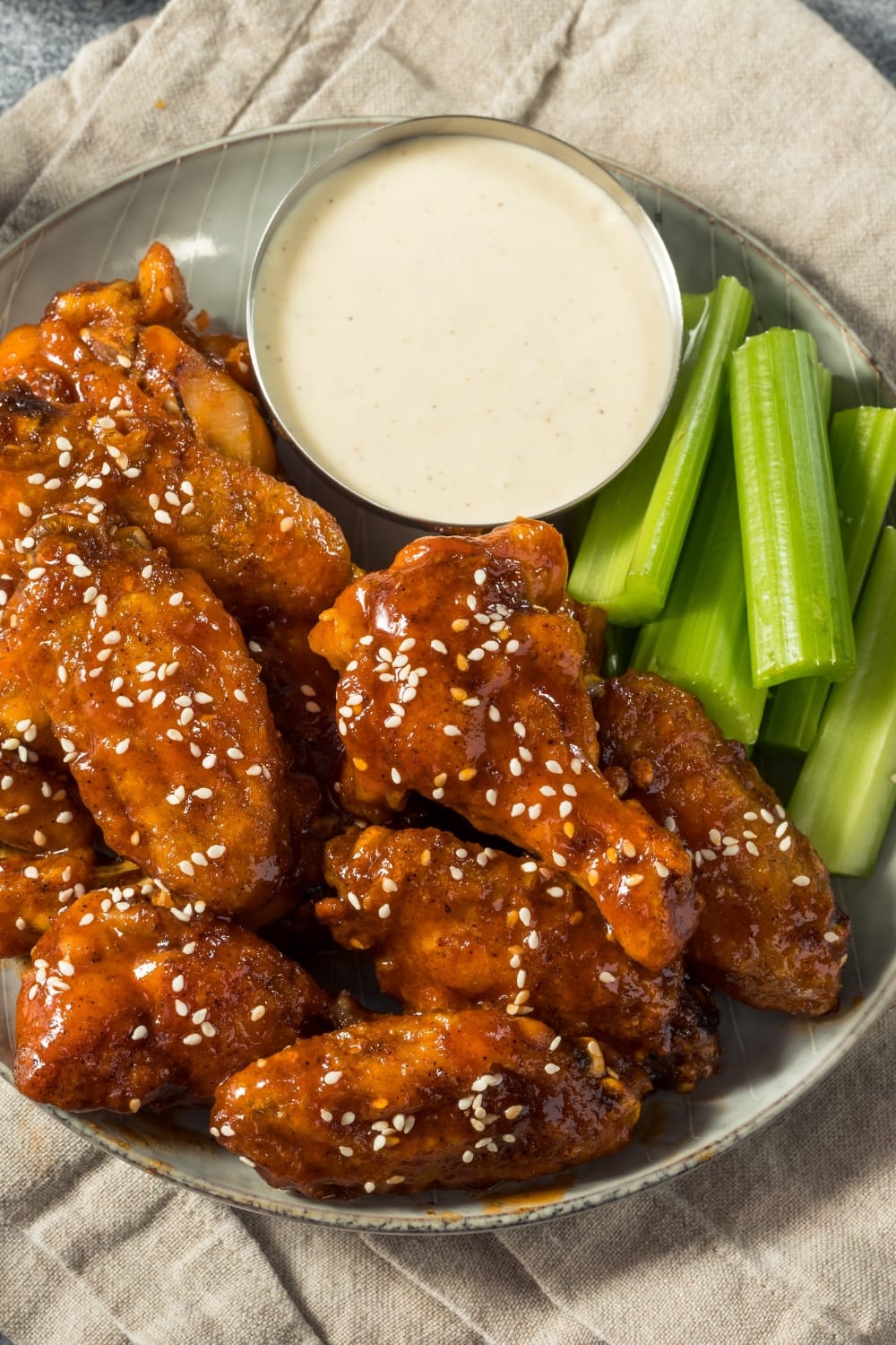 Chicken Wings with Sriracha Honey Garnished With Sesame Seeds Served With Slices of Fresh Celery Stalk and White Sauce Dip
