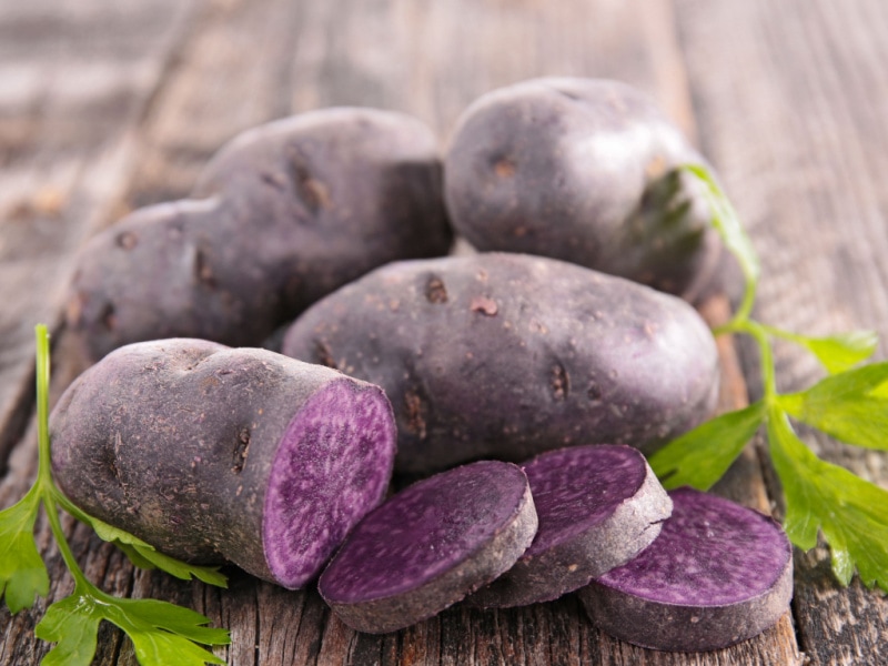 Whole and Sliced Purple Potatoes on Top of a Wooden Table