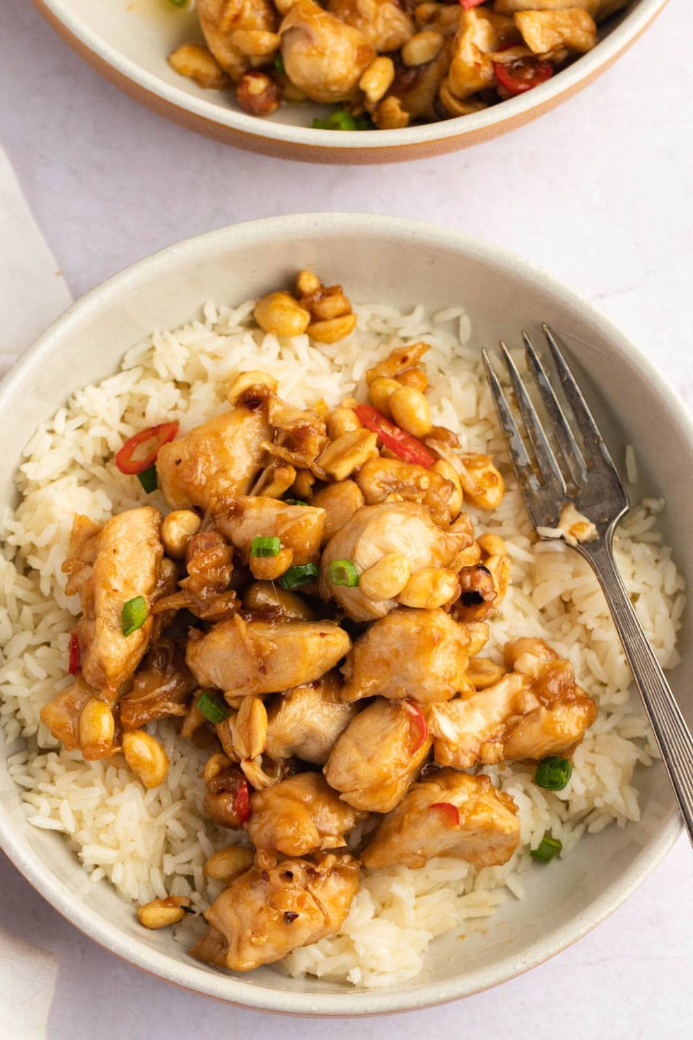 Bowl of Princess Chicken Served on Top of White Rice With Chopped Peanuts and Onion Leaves