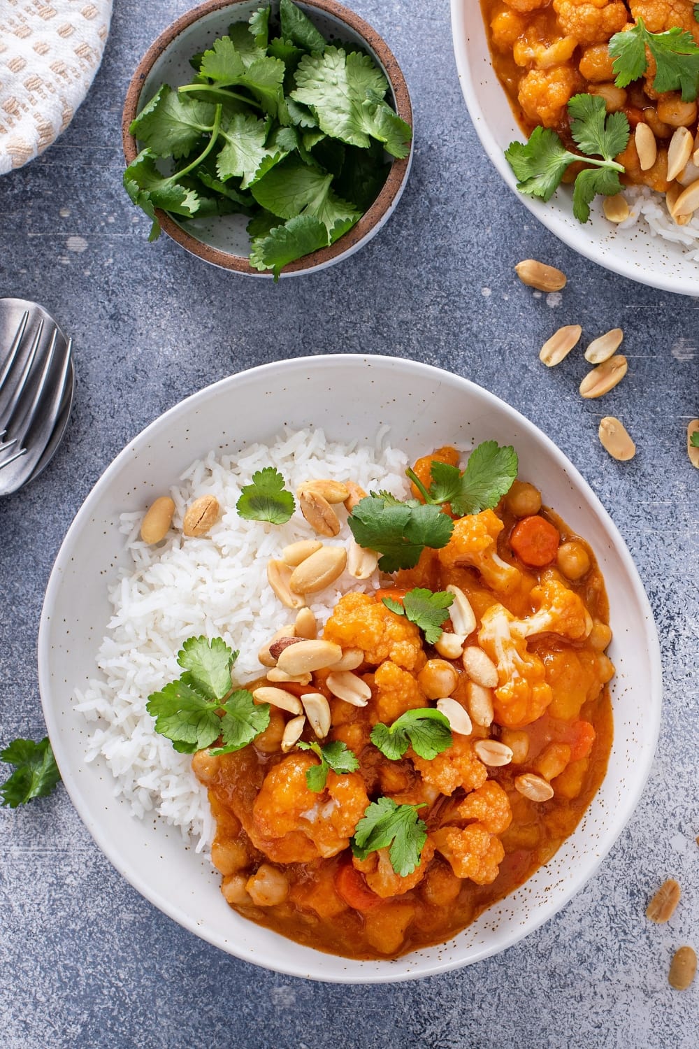 Cauliflower curry with chickpeas and carrots garnished with nuts and fresh parsley served with white rice on a plate