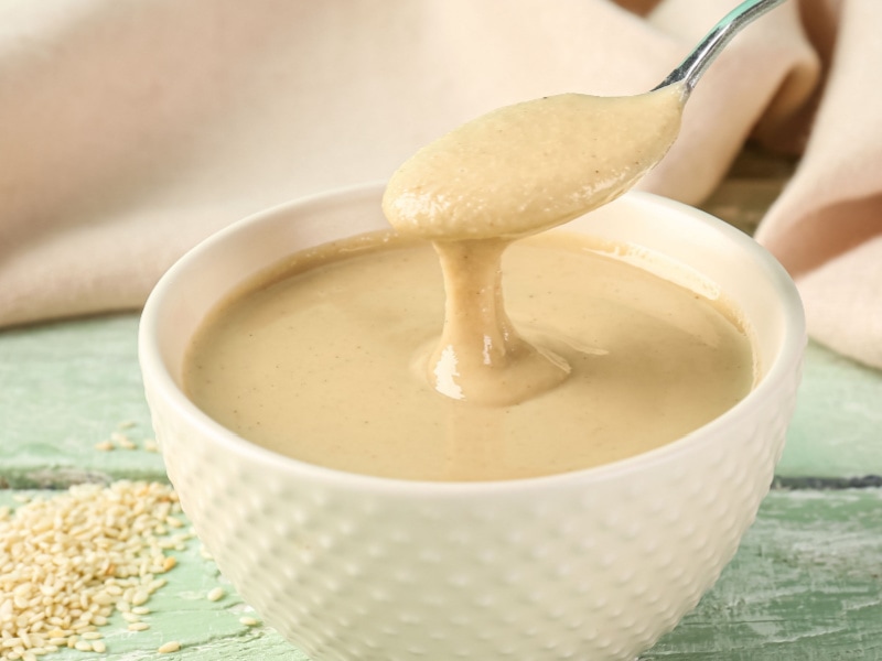 Spoon Dripping With Tahini Sauce From a White Bowl