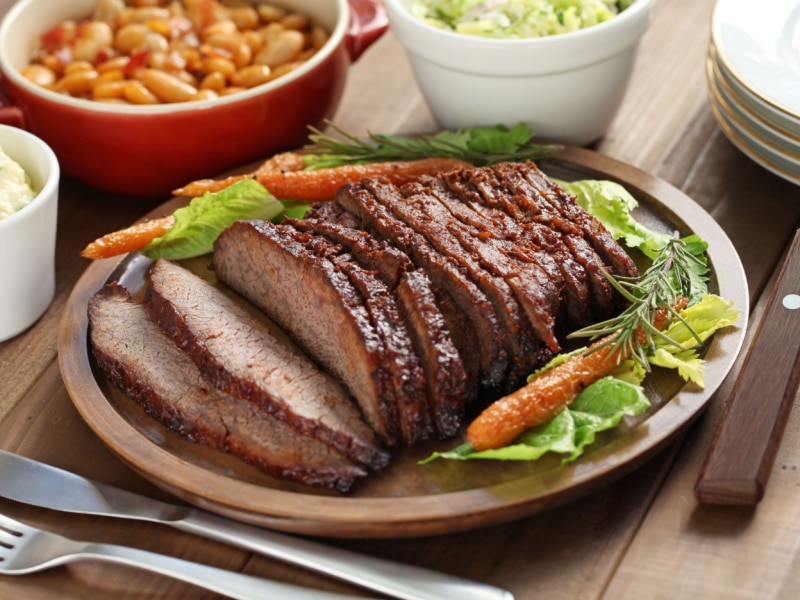 Smoked Beef Brisket Served on a Wooden Plate Garnished With Roasted Carrots, Rosemary and Lettuce