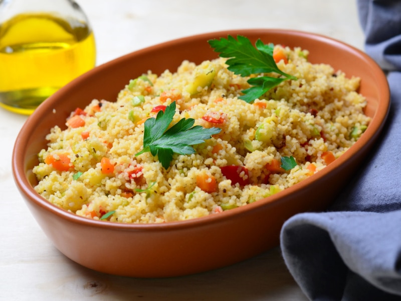 Cooked couscous served on a wooden bowl flavored with tomatoes, spices and herbs. 