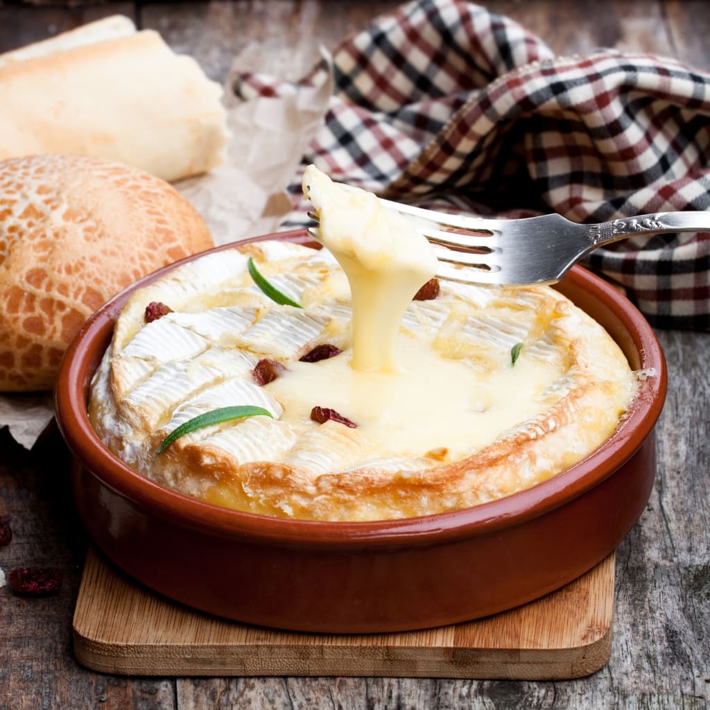 Spoon Scooping Melted Cheese Onto A Hot Baked Camembert Cheese Fondue From A Clay Bowl.