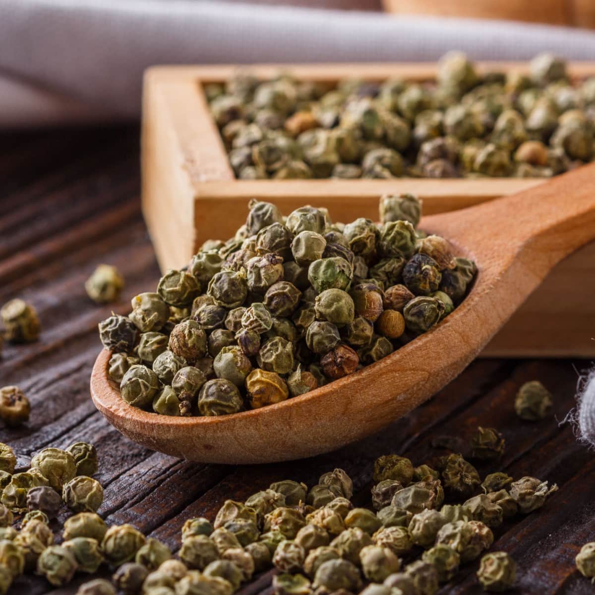 Dried Green Peppercorn in a Wooden Spoon with Peppercorns Spilling Out on the Wooden Table