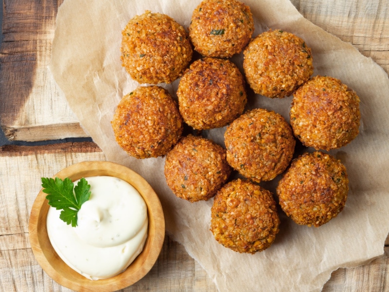 Falafel balls on a parchment paper served with white sauce on a wooden bowl. 