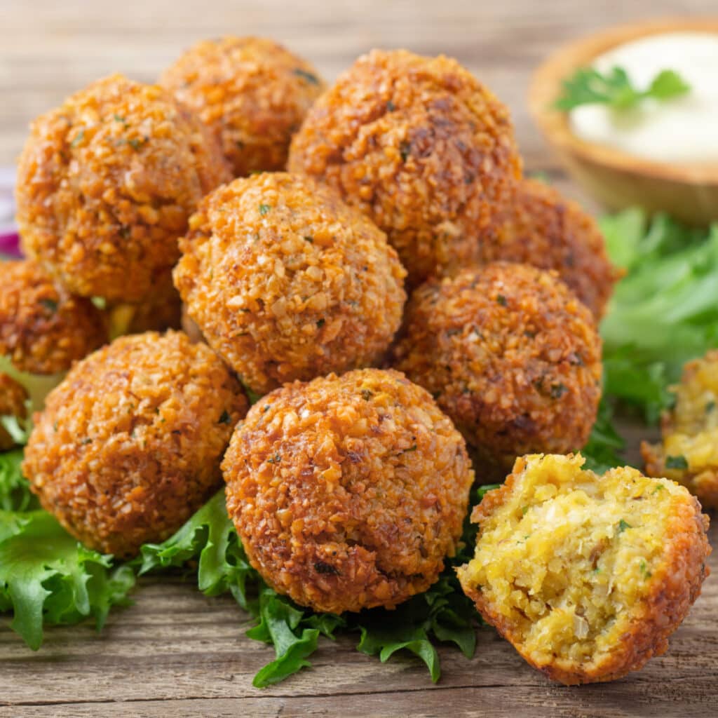 Crispy falafel balls laid on lettuce leaves served with white sauce on a wooden table.