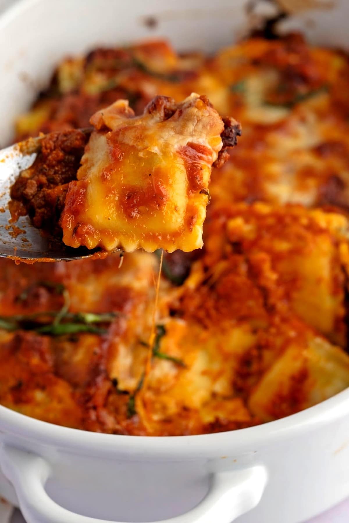 Ravioli Lasagna in a casserole dish, picking up one ravioli with a spoon