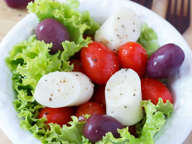 A bowl of heart of palm salad made with sliced heart of palm, olives, cherry tomatoes and lettuce. 