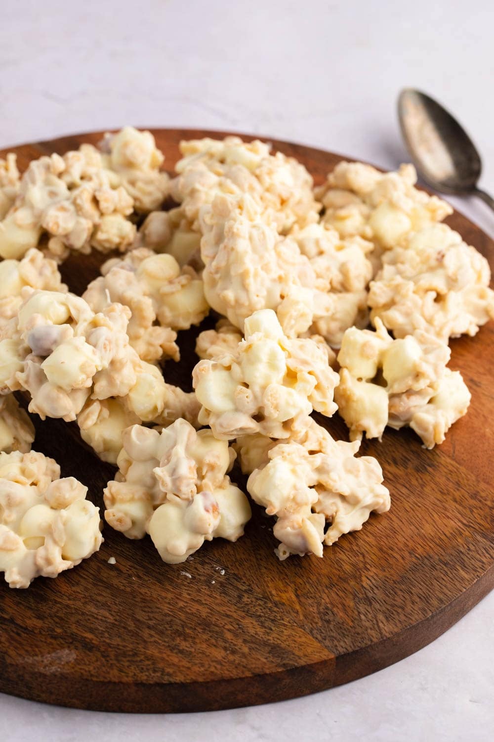 Rice Krispie Cookies covered with white chocolate with mini marshmallows and salted peanuts on a wooden cutting board.