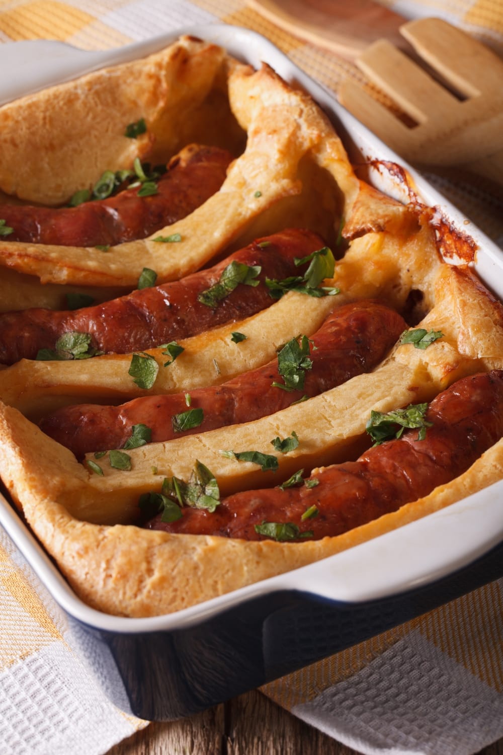 Toad in a Hole on a  Baking Dish Made With Dough and Sausage, Garnished With Chopped Herbs