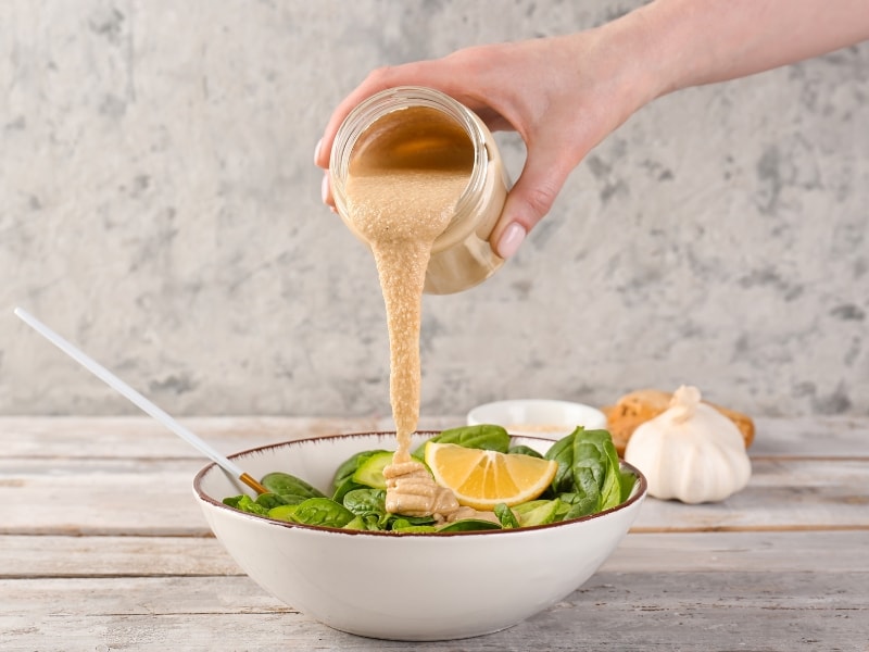 Woman Pouring Tahini Sauce into a Bowl of Salad