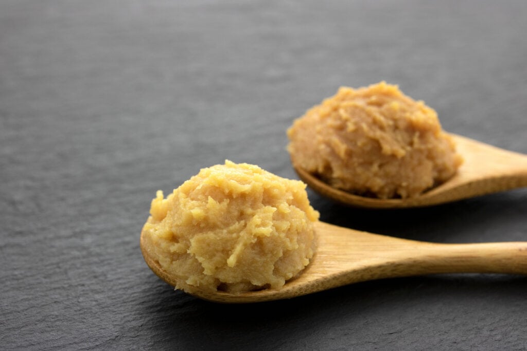 Two Wooden Spoon With Scoops of Miso Paste on Top of Black Concrete Table