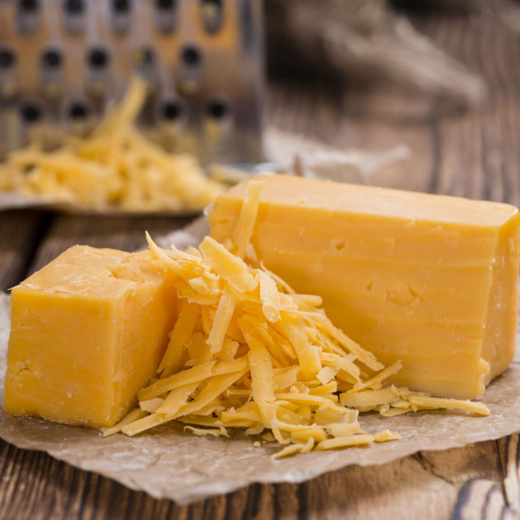 Slice and Grated Cheddar Cheese on a Parchment Paper