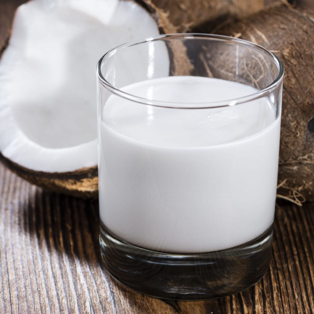 A Glass of Cream of Coconut and Coconuts on a Wooden Table