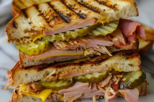 Close Up Cross Section of Halved Cuban Sandwich with Ham, Pork, Cheese, Pickles, and Mustard