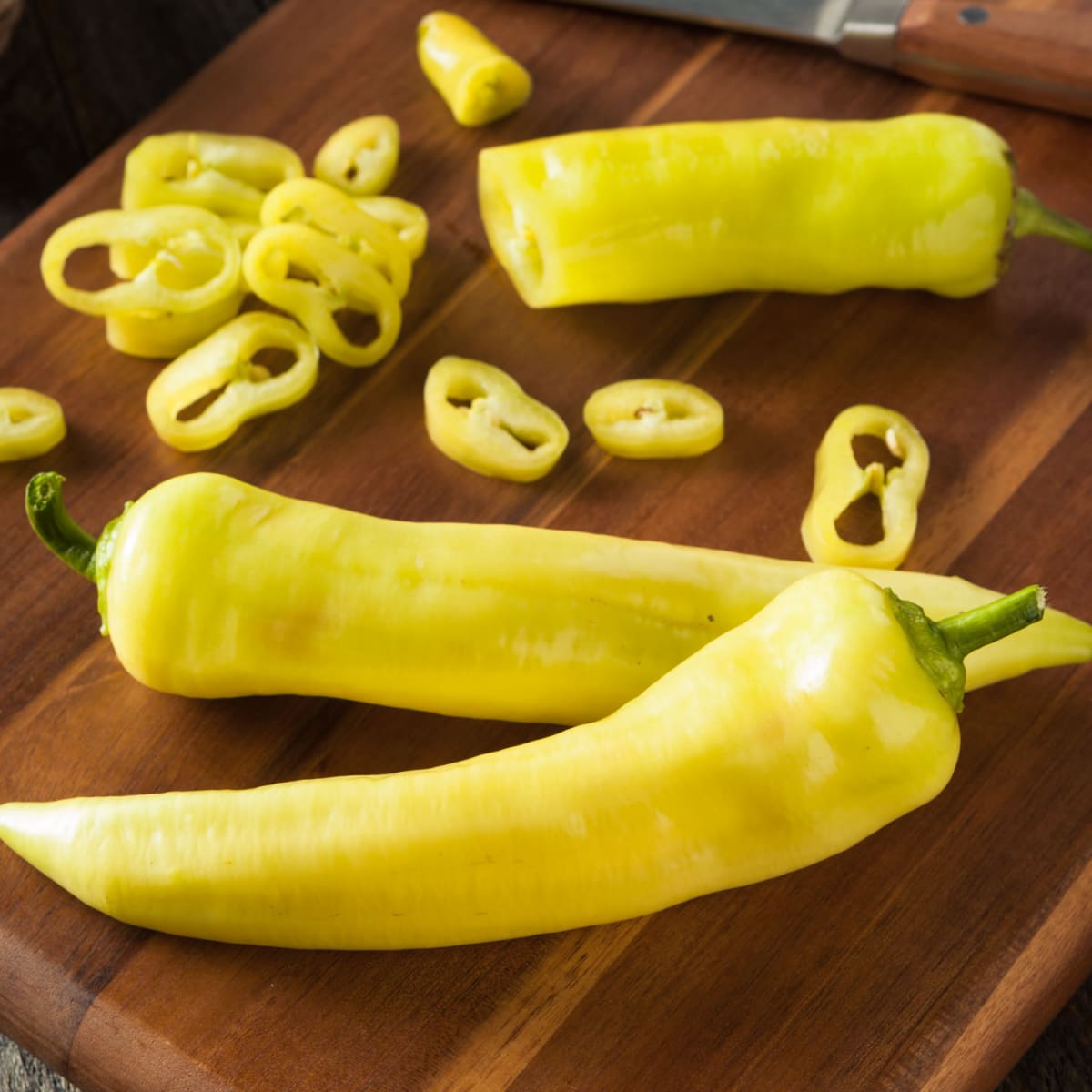 Whole and Slice Banana Peppers on a Wooden Cutting Board